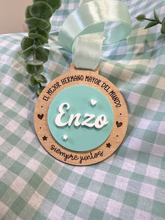 Medalla de hermano mayor de madera con nombre Enzo en metacrilato blanco sobre círculo turquesa y lazo mint, Lunera